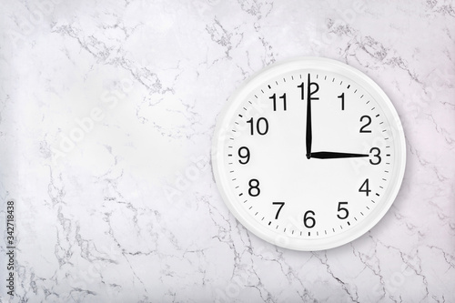 White round wall clock on white natural marble background. Three o'clock. 3 a.m. or 3 p.m