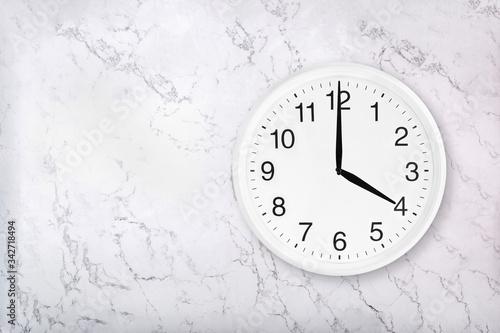 White round wall clock on white natural marble background. Four o'clock. 4 a.m. or 4 p.m