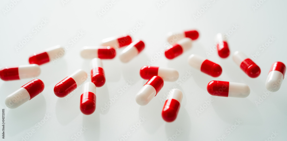 Many red and white capsules pill spread on white background with shadow. Global healthcare concept. Antibiotics drug resistance. Antimicrobial capsule pills. Pharmaceutical industry. Many red and white capsules pill spread on white background with shadow. Global healthcare concept. Antibiotics drug resistance. Antimicrobial capsule pills. Pharmaceutical industry.