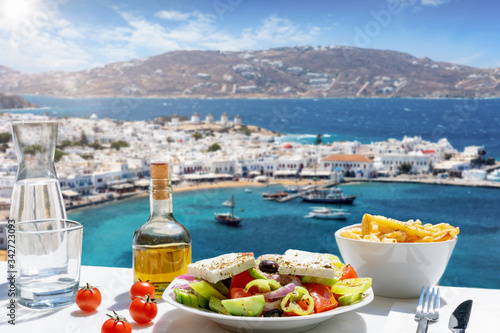 Konzept der griechischen Küche mit Bauernsalat und Olivenöl vor der atemberaubenden Aussicht auf die Stadt der Insel Mykonos, Griechenland