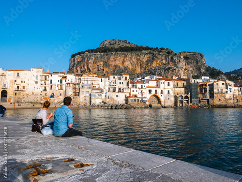 Cefalù, Palermo, Sicily - Boy and girl sitting on the dock and admiring the beautiful seascape.