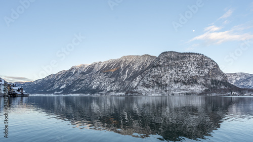 Snowy Austrian village Hallstatt by lake during sunset hour with clouds in winter
