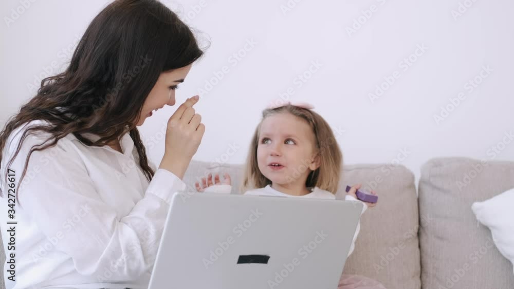 The pretty mother and her child girl are studying with a laptop. The mother is teaching heer kid. The girl is getting along with the parent typing on the keyboard and watching something on hte laptop The pretty mother and her child girl are studying with a laptop. The mother is teaching heer kid. The girl is getting along with the parent typing on the keyboard and watching something on hte laptop