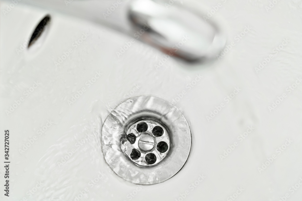 Water flowing down from faucet to sink, view from above, detail on silver tap hole Water flowing down from faucet to sink, view from above, detail on silver tap hole