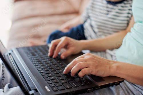 Close up of mother's hand typing on keyboard while baby is leaning on her