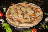Pizza with prawns frutti di mare - on a black table, with scattered spices and ingredients. Photo for the menu.