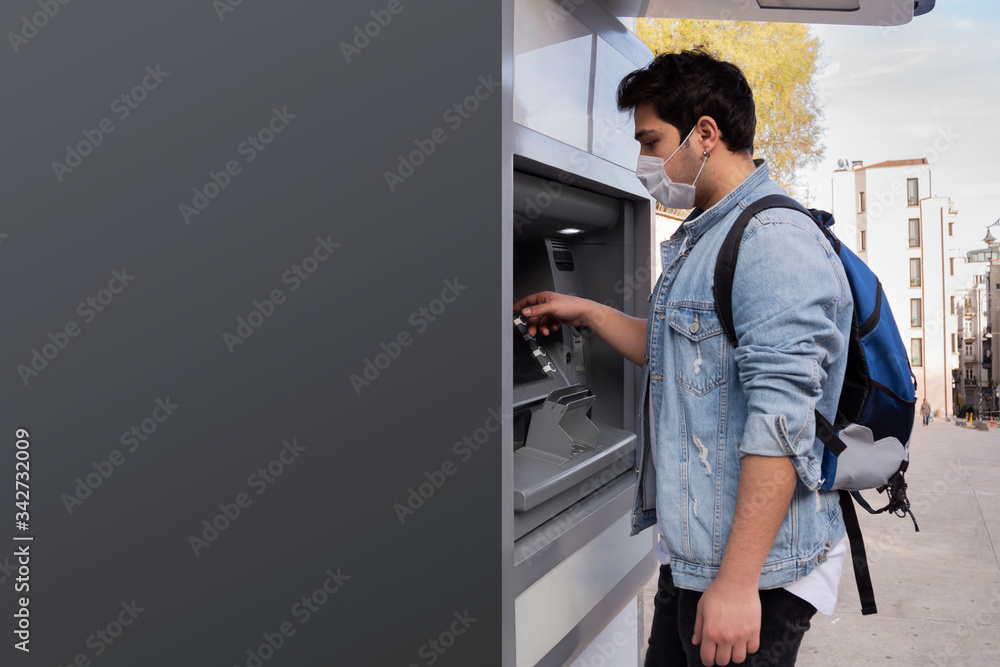 The young man performs his transactions from the bank atm using his protective mask.