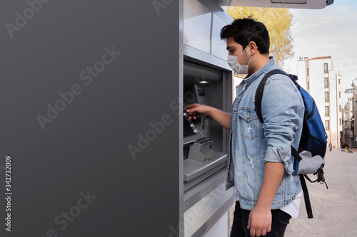 The young man performs his transactions from the bank atm using his protective mask.