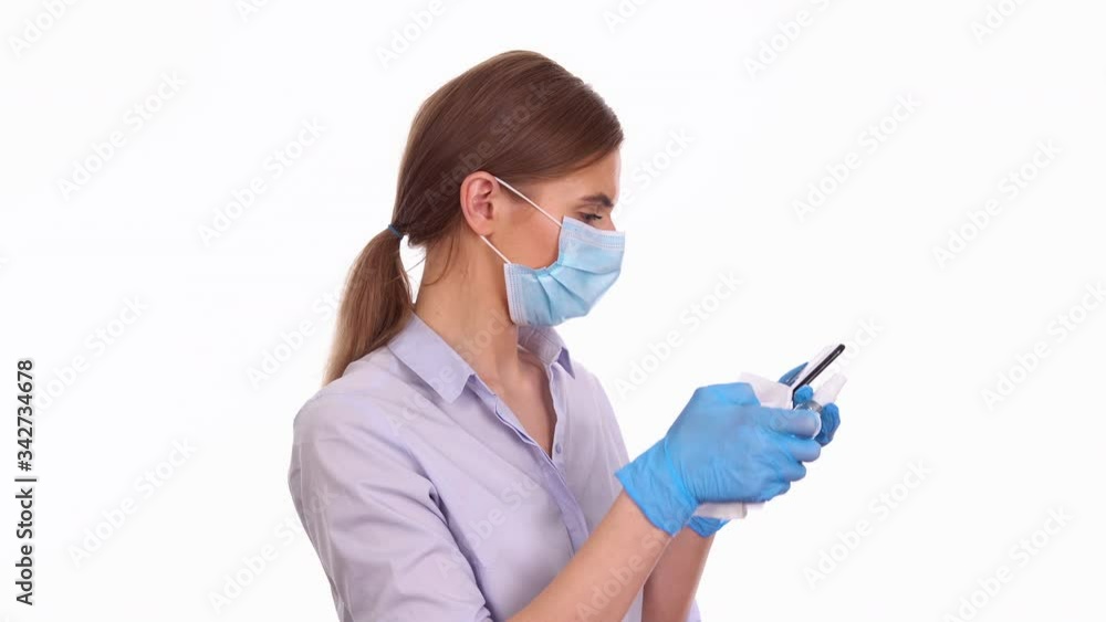 Young woman disinfecting smartphone with antiseptic spray, COVID-19 protection concept Young woman disinfecting smartphone with antiseptic spray, COVID-19 protection concept