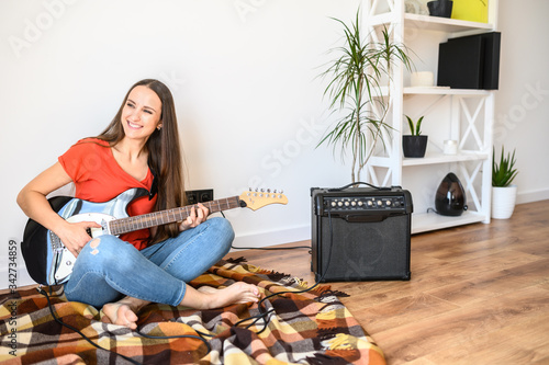 A young positive woman spends home leisure playing an electric guitar. Hobby concept, talent photo