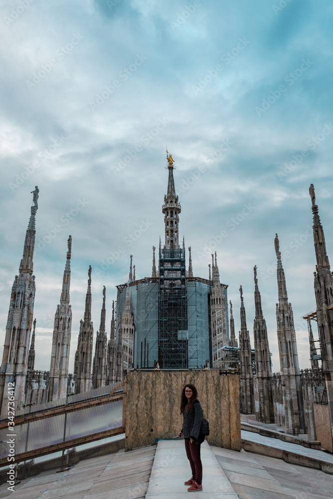 Young woman looking at camera on the rooftop terrace of Milan Cathedral with the pinnacle of the Madonnina in the background