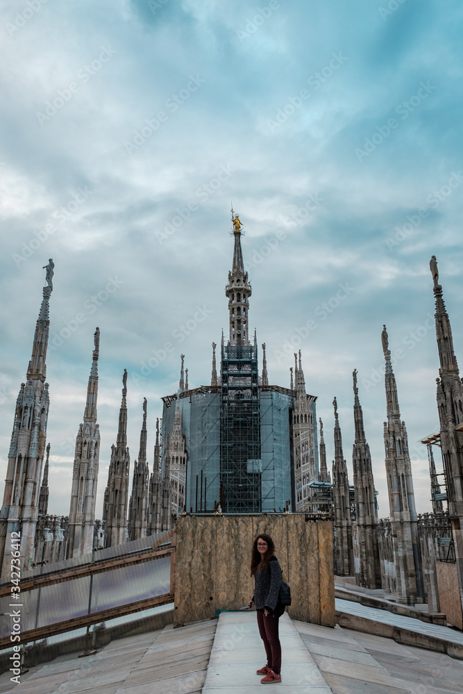 Young woman looking at camera on the rooftop terrace of Milan Cathedral with the pinnacle of the Madonnina in the background Young woman looking at camera on the rooftop terrace of Milan Cathedral with the pinnacle of the Madonnina in the background