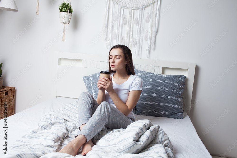 Wake up in bed in the morning and drink coffee. Young beautiful girl sitting on the bed Wake up in bed in the morning and drink coffee. Young beautiful girl sitting on the bed