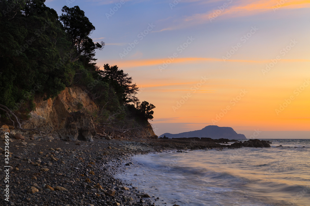 Sunset over a stony beach and coastal cliffs on the Coromandel Peninsula, New Zealand