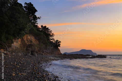 Sunset over a stony beach and coastal cliffs on the Coromandel Peninsula, New Zealand