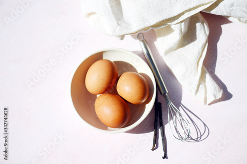 Overhead view of eggs, vanilla and whisk on table