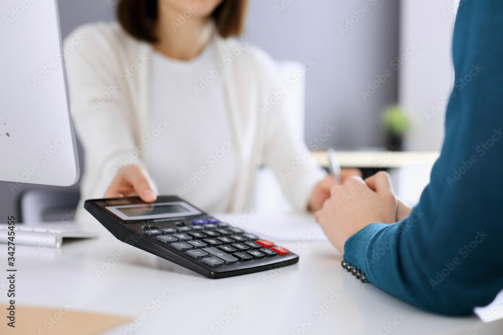 Accountant checking financial statement or counting by calculator income for tax form, hands closeup. Business woman sitting and working with colleague at the desk in office toned in blue. Tax and Accountant checking financial statement or counting by calculator income for tax form, hands closeup. Business woman sitting and working with colleague at the desk in office toned in blue. Tax and