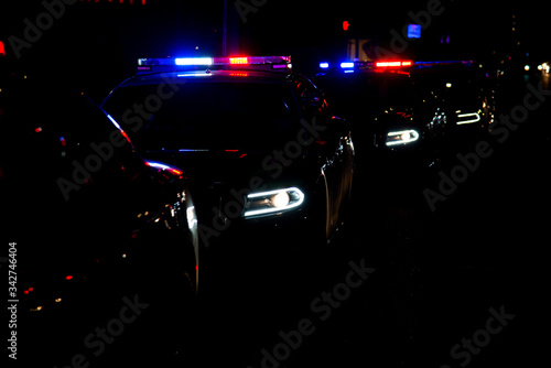 Police cars lined up on the street with their emergency lights on. (A faster shutter speed was used to darken the ambient light)
