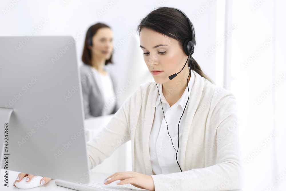 Call center. Casual dressed woman sitting in headset at customer service office. Group of operators at work. Business concept Call center. Casual dressed woman sitting in headset at customer service office. Group of operators at work. Business concept