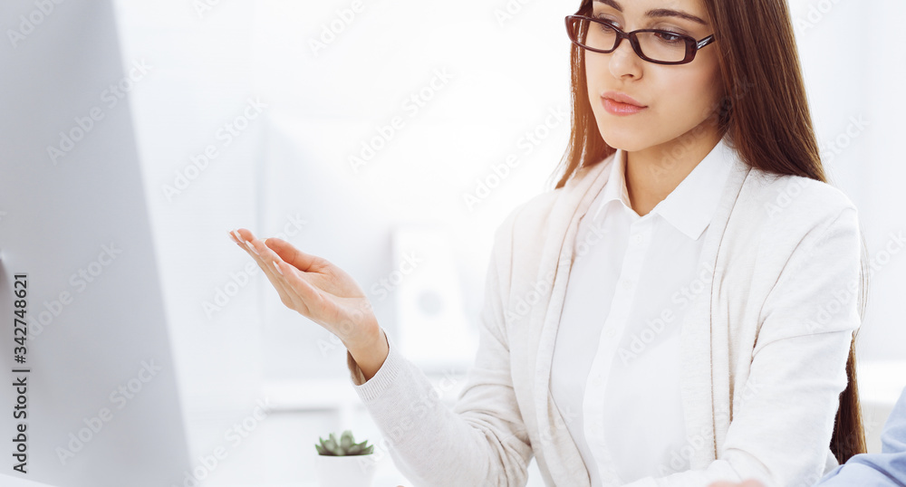 Beautiful young woman sitting at the desk with computer in sunny office. Looks like student girl or business lady communicating with casual dressed man Beautiful young woman sitting at the desk with computer in sunny office. Looks like student girl or business lady communicating with casual dressed man