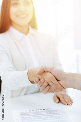 Casual dressed businessman and woman shaking hands after contract signing in sunny office. Handshake concept