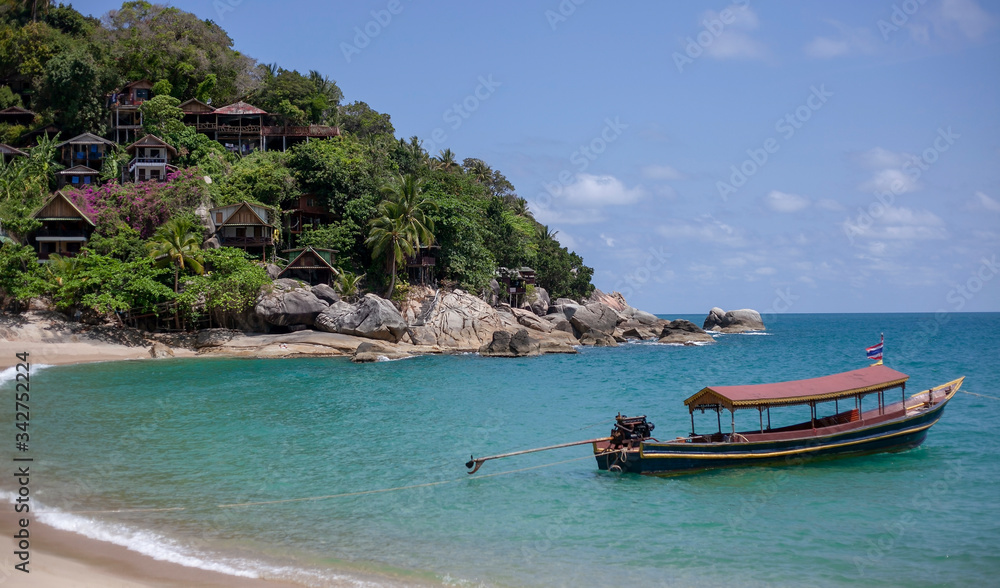 Small houses on the mountain in the jungle and a boat on the beach in Thailand on the island of Phangan. Natural background with blue sea.
