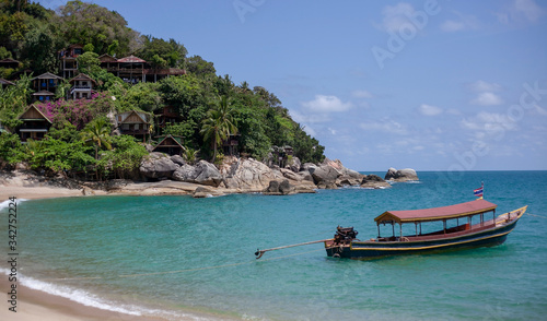 Small houses on the mountain in the jungle and a boat on the beach in Thailand on the island of Phangan. Natural background with blue sea.