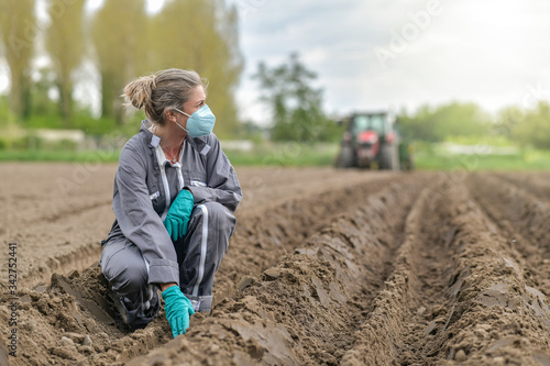 Female farmer  analyses the soil before planting and wearing a protective mask against coronavirus © ElitProd