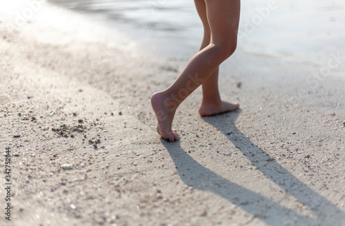 Little feet of a child walk on a sandy beach in the evening.
