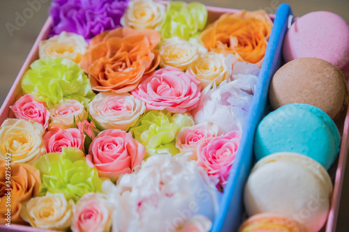 Close up view of gift box with flowers and colorful macaroons at flower shop. Floristry, handmade, wedding, birthday, dessert, biscuit, sweet food and traditional french cuisine concept