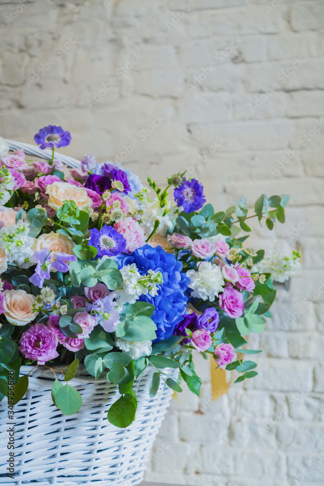 Large floral basket with colorful flowers against brick wall at workshop, flower shop. Floristry, holiday, romantic, celebration, handmade and small business concept
