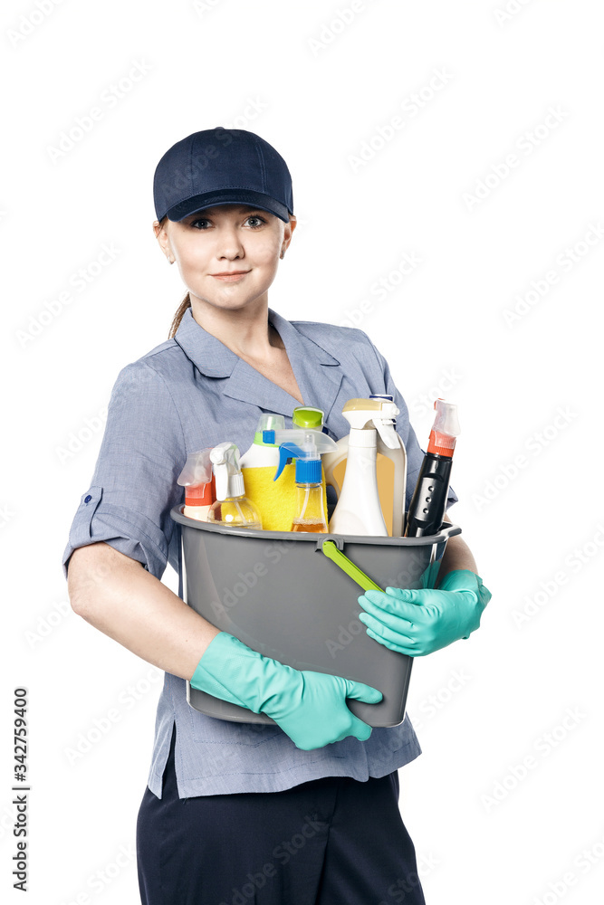 Attractive young woman in cleaning uniform and rubber gloves holding a bucket of cleaning products in her hands, isolated on white background Attractive young woman in cleaning uniform and rubber gloves holding a bucket of cleaning products in her hands, isolated on white background