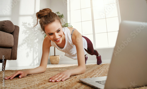 Young woman doing abdominal exercise in room with laptop.