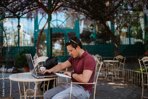 A young caucasian man is working on a computer in a cafe garden