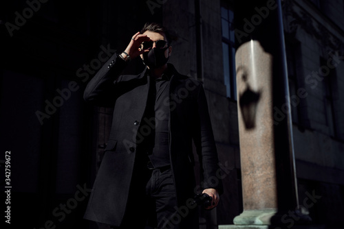  man in a black suit and a black medical mask walks through the city's historic streets during the quarantine