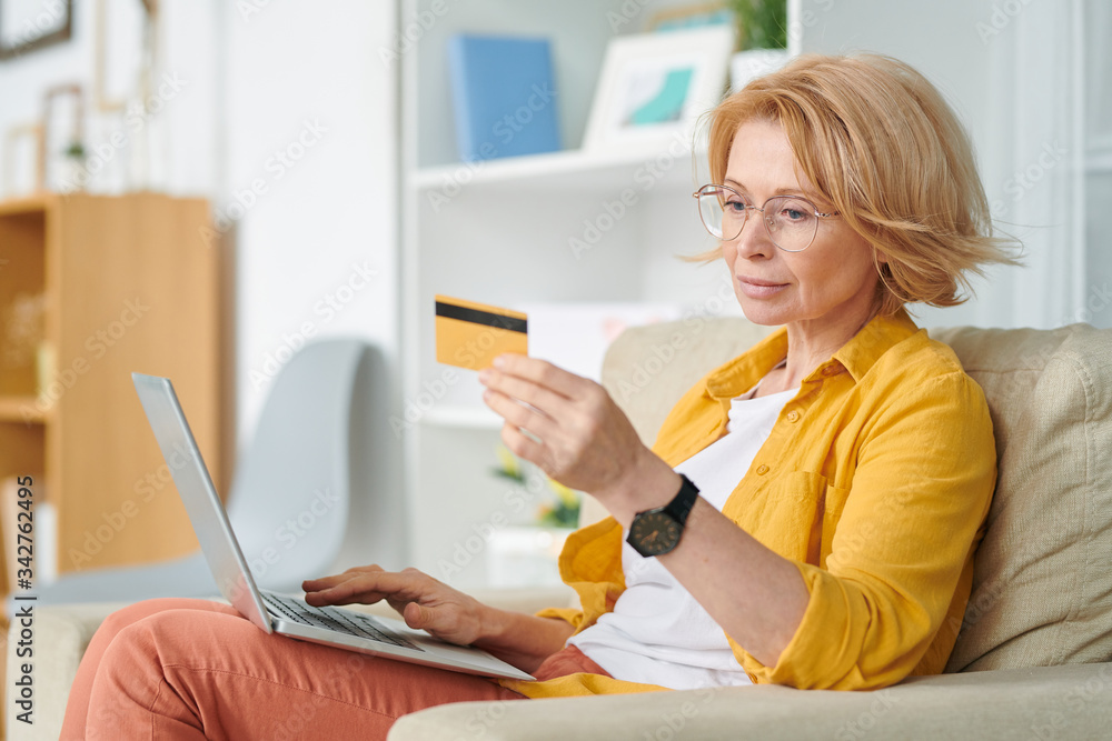 Pretty blond female looking at credit card while going to buy food online Pretty blond female looking at credit card while going to buy food online