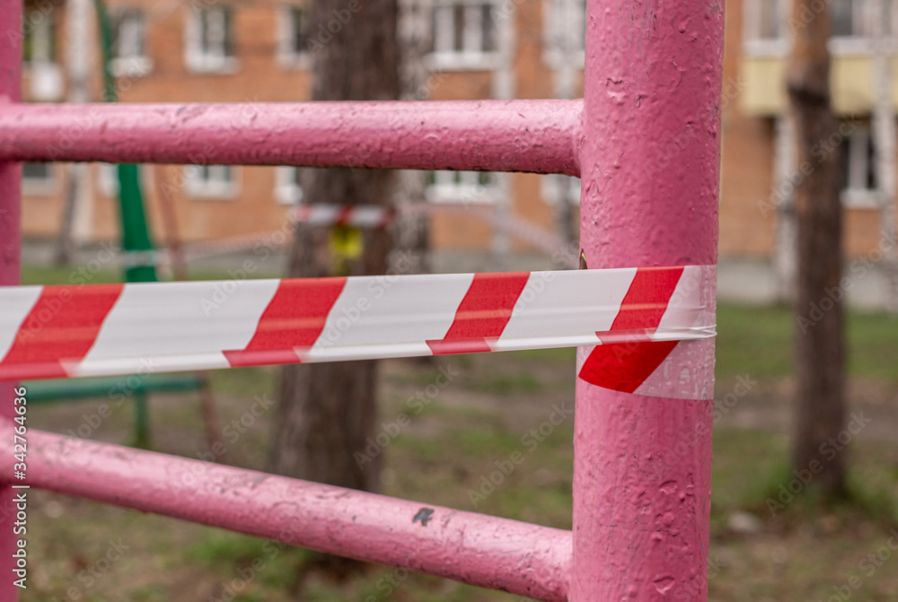 A white and red ribbon prohibits entry to the Playground. Playground swing in the open air prohibiting red tape, infection prevention