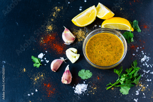 A moroccan or middle eastern marinade, Chermoula, set against a black dark background and surrounded by the ingredients used to make the sauce. photo