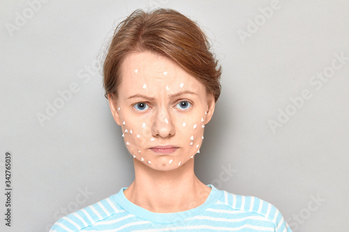 Portrait of sad unhappy girl with white drops of face cream on skin