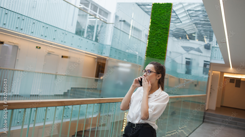 Phone conversation, a young emotional woman in a white shirt and glasses talking on a mobile phone