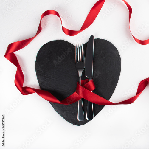 Valentine's Day love romantic dinner setup on white background, red ribbon, black heart shaped plate and flowers