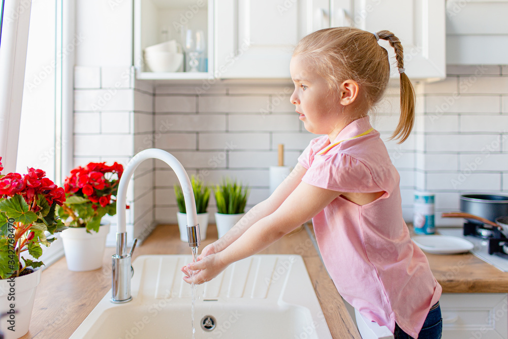 Blonde toddler girl washing hands in the lingh kitchen before eating. Hygiene and healthcare concept. Blonde toddler girl washing hands in the lingh kitchen before eating. Hygiene and healthcare concept.