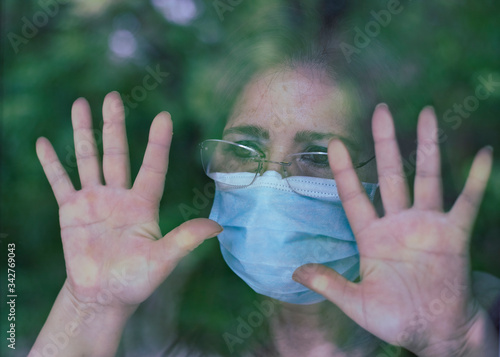 Photography woman with depressed face mask at home window covid-19