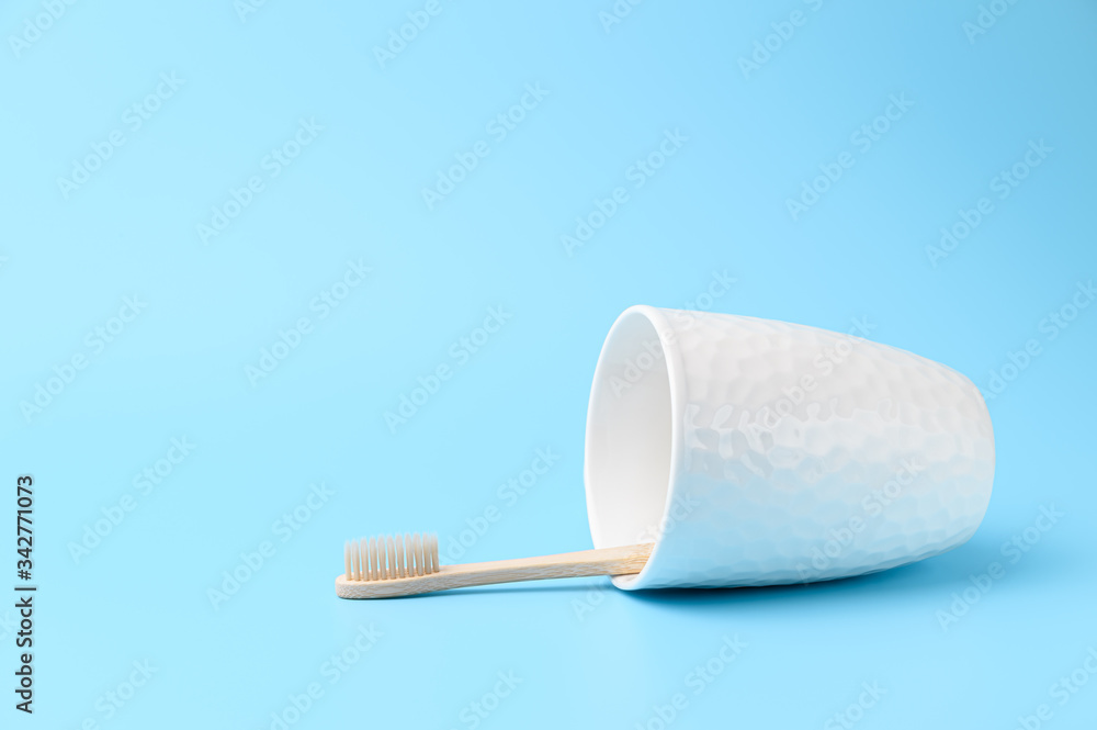 Fototapeta premium A bamboo toothbrush in a white glass lies on a light blue background. Zero waste and without plastic concept. Copy space, horizontal orientation.