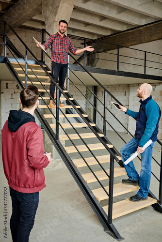 Happy young foreman in casualwear talking to his team on staircase