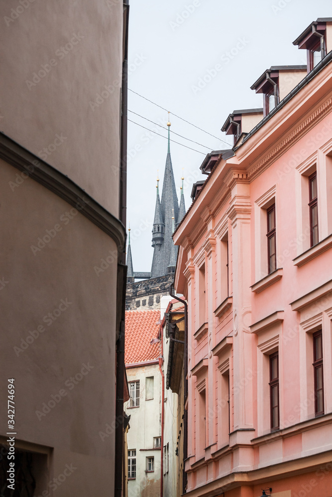 Narrow street with medieval buildings and cobblestones in the old town of Prague, also called Stare mesto, with the top of the clocktower of Staromestska radnice visible in background