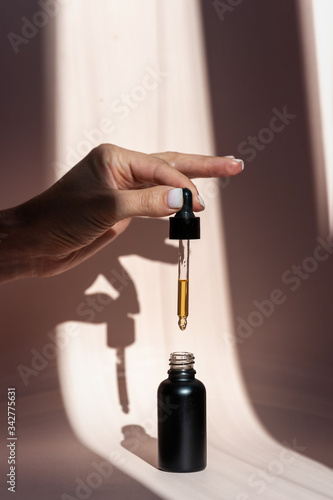 Woman holding pipette with natural oil over glass bottle