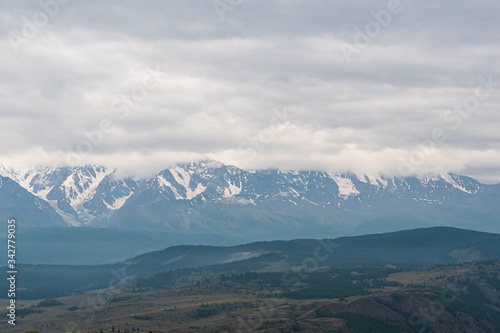 snow peaks on horizon  ridge of rocks under cloudy sky in mountain valley