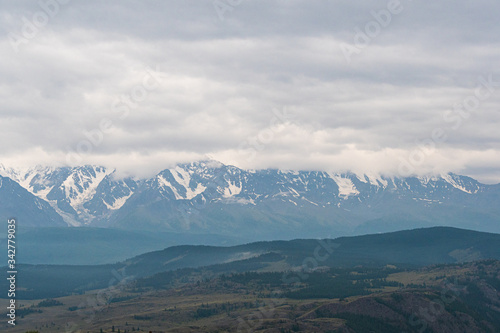 snow peaks on horizon, ridge of rocks under cloudy sky in mountain valley