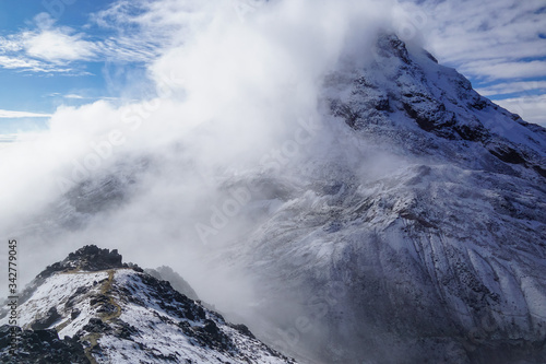 ILINIZA VOLCANO, ECUADOR - DECEMBER 04, 2019: View from the north peak towards the snow covered south peak emerging from the mist 